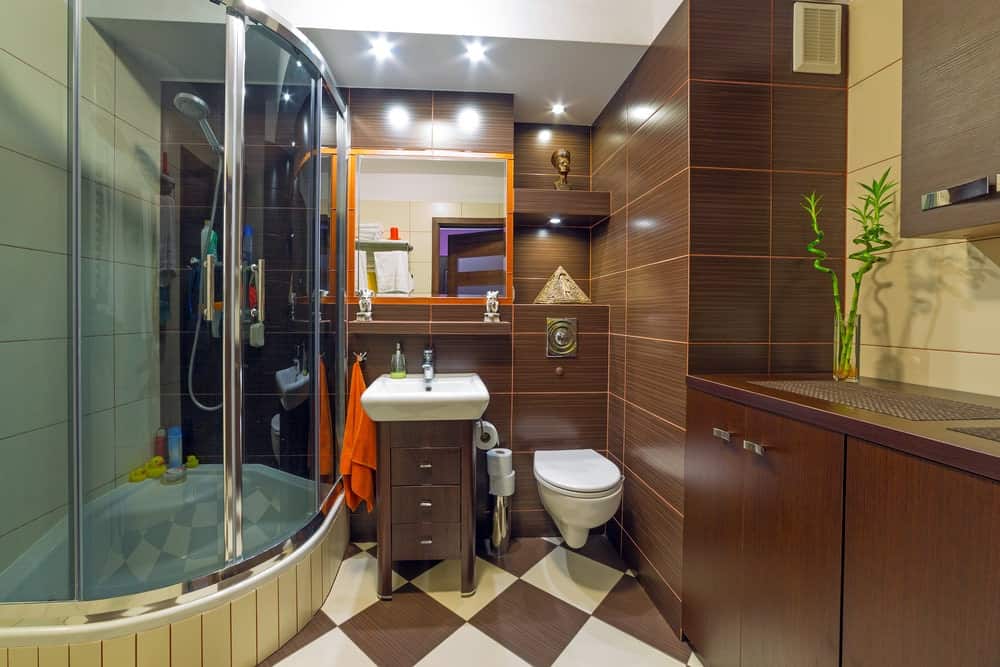小主浴室，棕色格子瓷砖地板和棕色瓷砖墙壁。它还提供了一个时尚的步入式淋浴间。