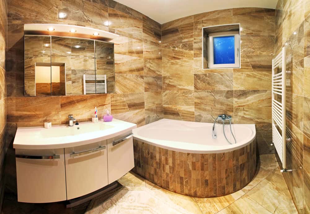 小主浴室设有一个时尚的洗手台和角落的浴缸，周围是棕色的瓷砖墙壁和地板。