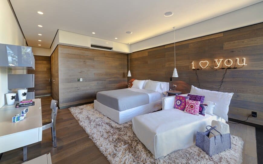主卧室的棕色木墙与硬木地板相匹配，上面铺着地毯。房间内有一张书桌和一张舒适的床。