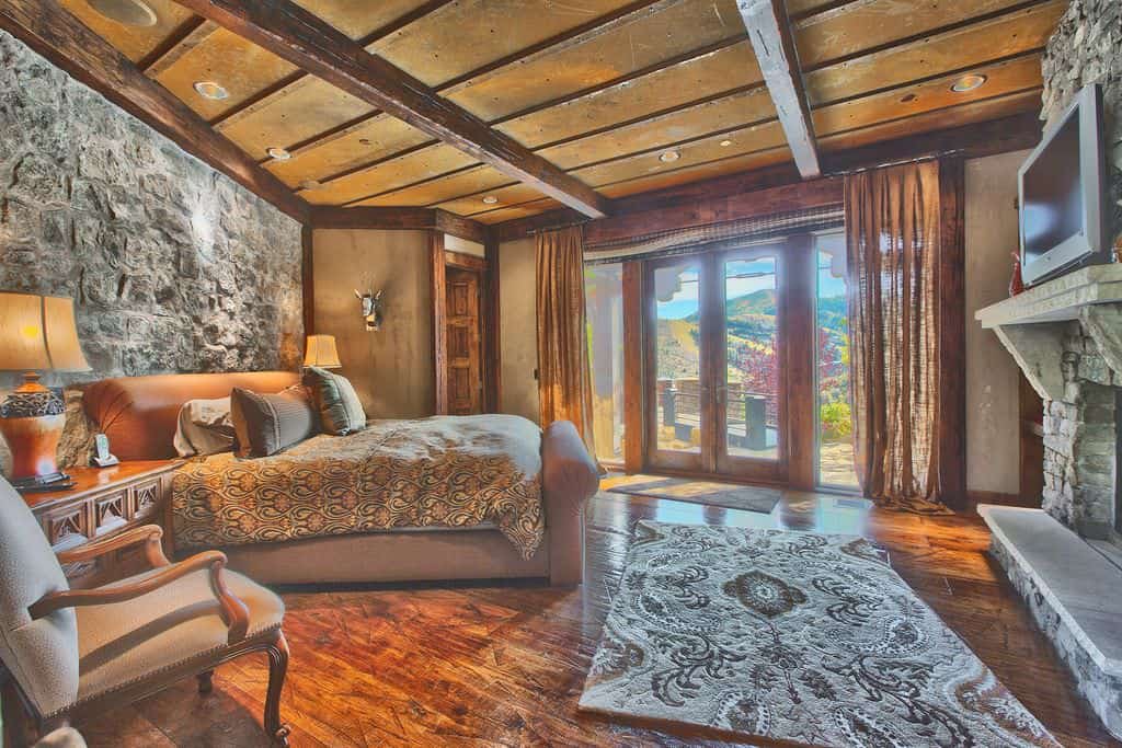 这间主卧室以硬木地板和棕色天花板为特色。房间里有一张舒适的床和一座壁炉，还有一条时尚的地毯。