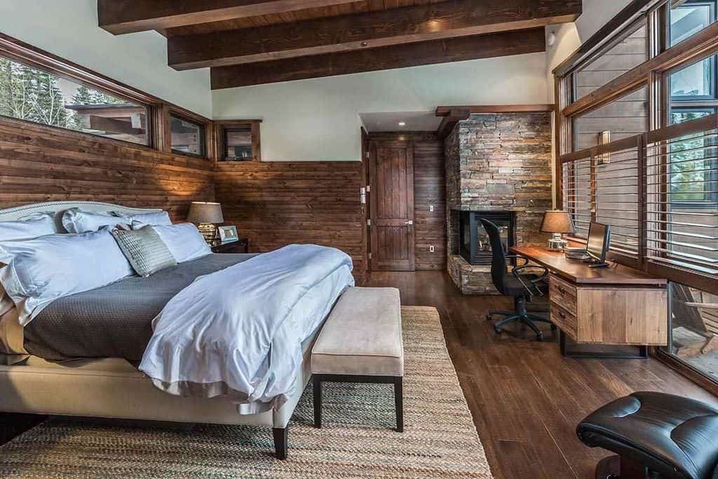 乡村风格的主卧室设有一张大床，上面铺着硬木地板。有一张办公桌和一座壁炉。