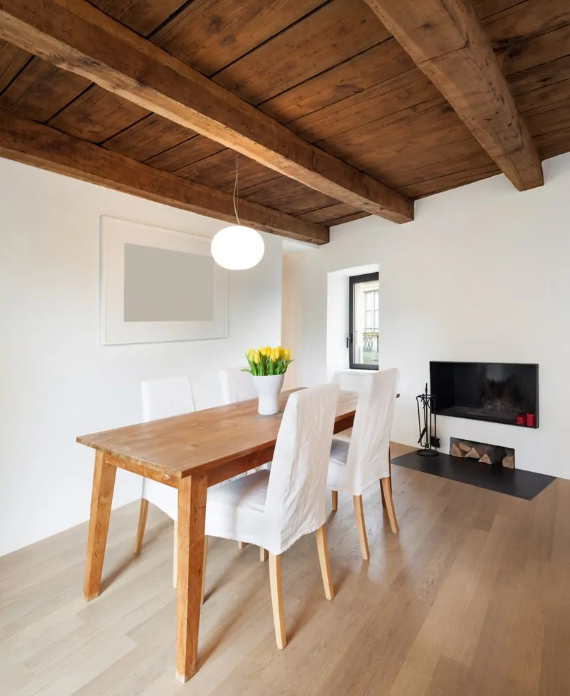 舒适的餐厅和一个现代壁炉在餐桌搭配白色的椅子。它有硬木地板和木梁天花板上挂着一个吊灯。