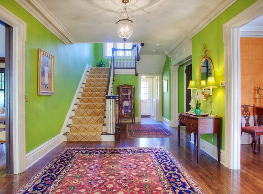 绿色的门厅设有硬木地板，上面有一个大的优雅的地毯和铺着地毯的楼梯。