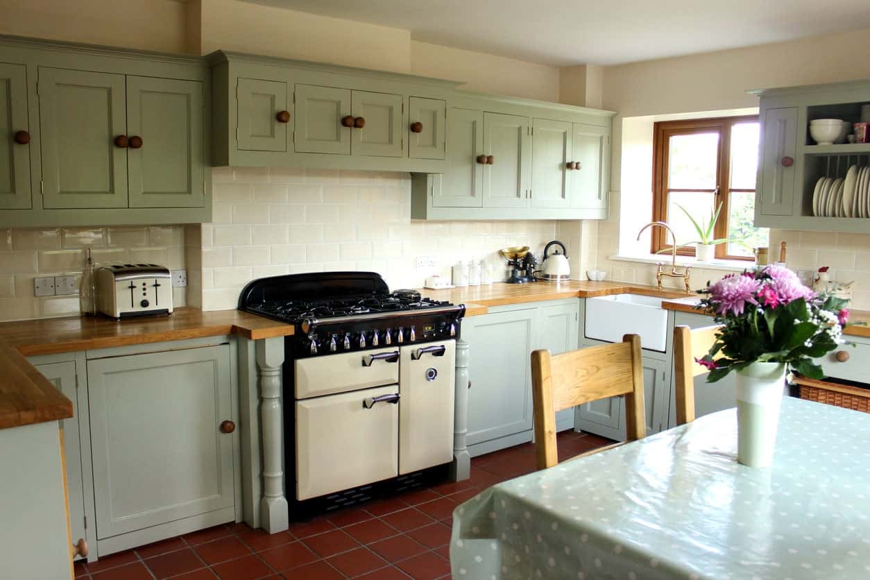 一个小厨房区域，有红色的瓷砖地板和绿色的橱柜和厨房柜台。