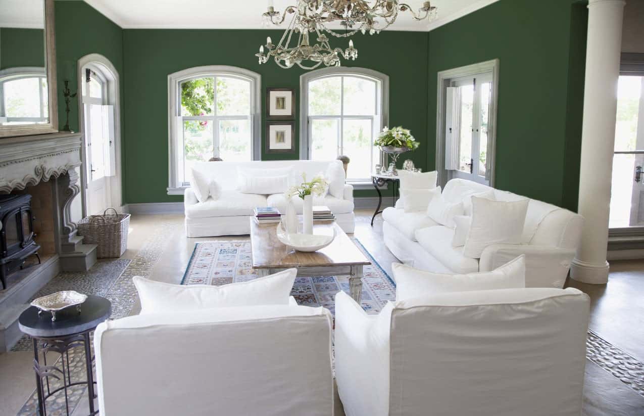客厅里有白色座椅和一个大壁炉，绿色的墙壁被一盏华丽的吊灯照亮。