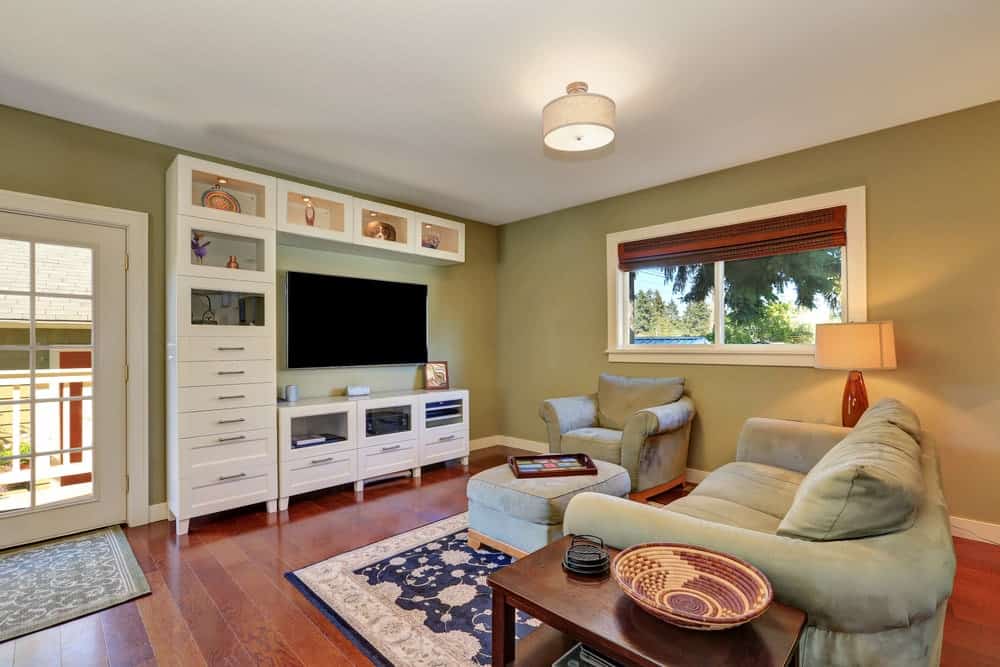 这间客厅提供了一张漂亮的沙发和一把椅子，在绿色墙壁上的宽屏电视前有一个搁脚凳。