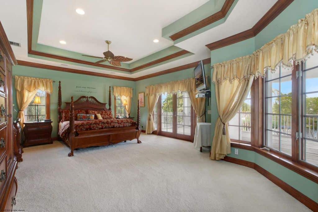 宽敞的主卧室，绿色的墙壁和棕色的口音。房间里有一张大床，地毯地板和托盘天花板。