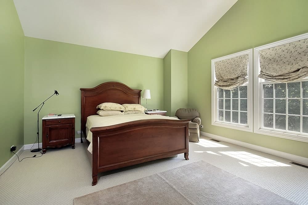 传统的木床有一个内置的木制床头板，与牛油果绿色的墙壁形成了很好的深色对比。这些绿色的墙壁与白色的棚屋天花板和白色编织地毯地板搭配得很好。