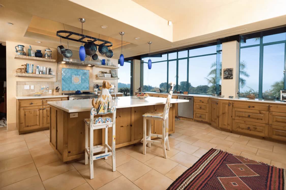西南厨房设有木制橱柜和早餐岛，配有动物柜台椅，以及一个黑色的锅架和俯瞰室外风景的全景窗户。
