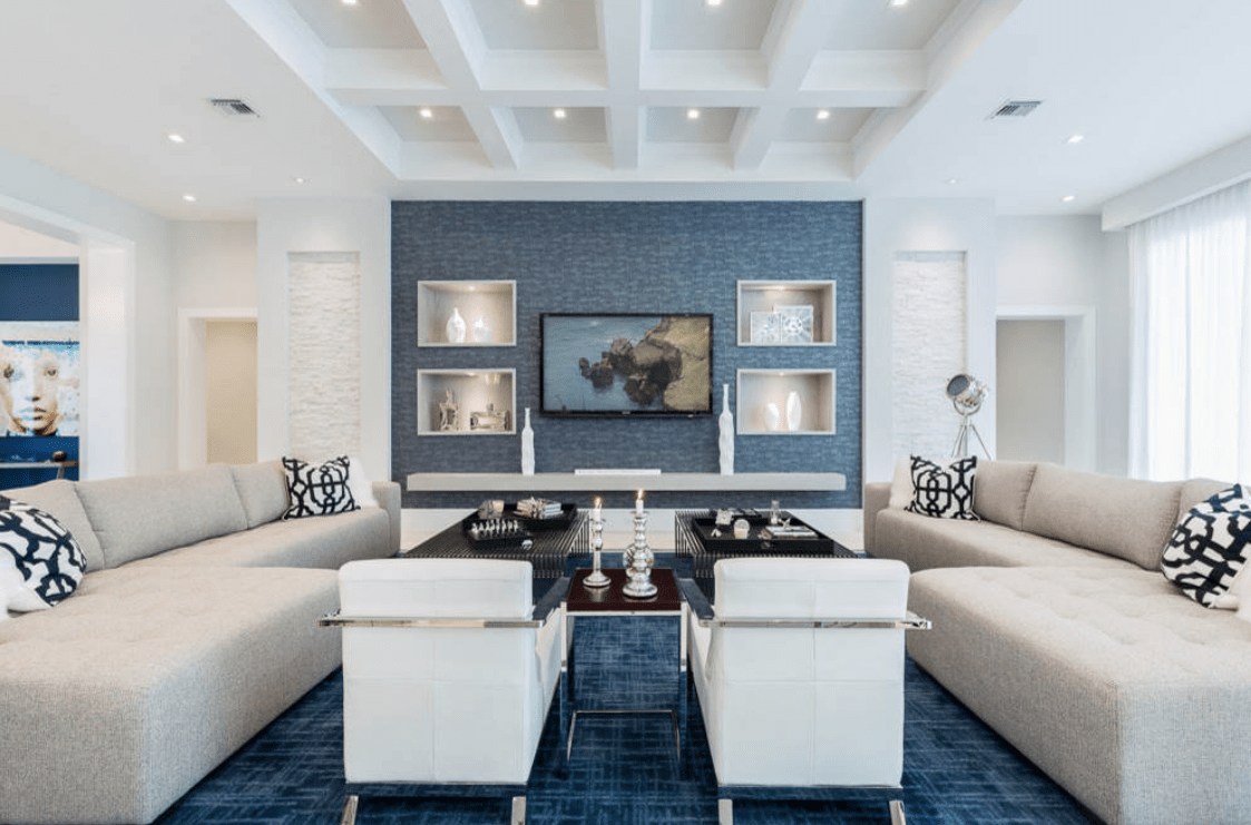 现代客厅的特色是格子天花板和深蓝色的强调墙，配有嵌入的架子，里面装满了可爱的框架和花瓶。