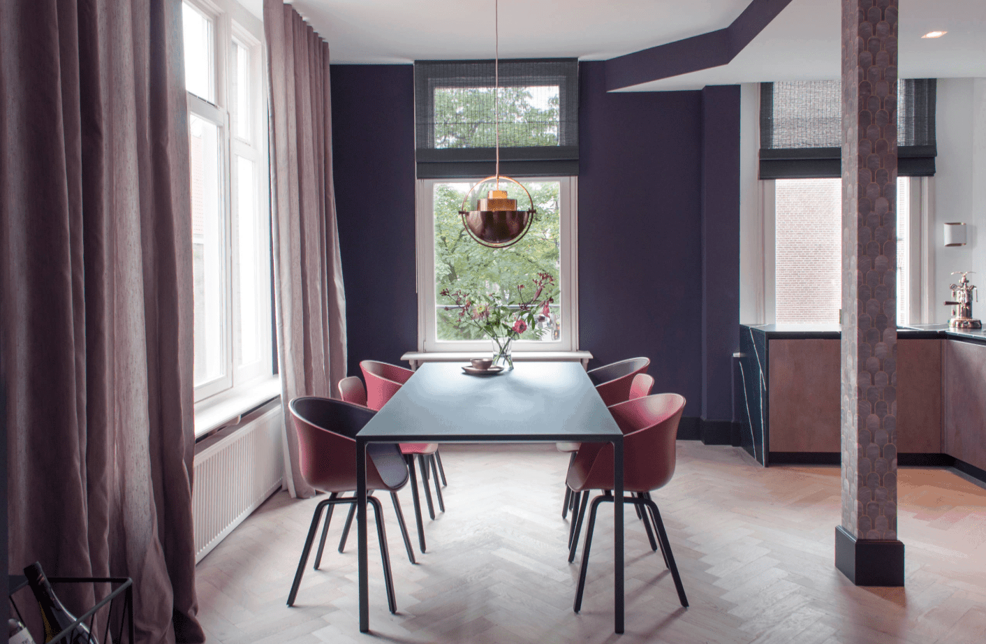 人字形地板上的长方形餐桌。这个区域被紫色的墙壁和窗帘包围着。