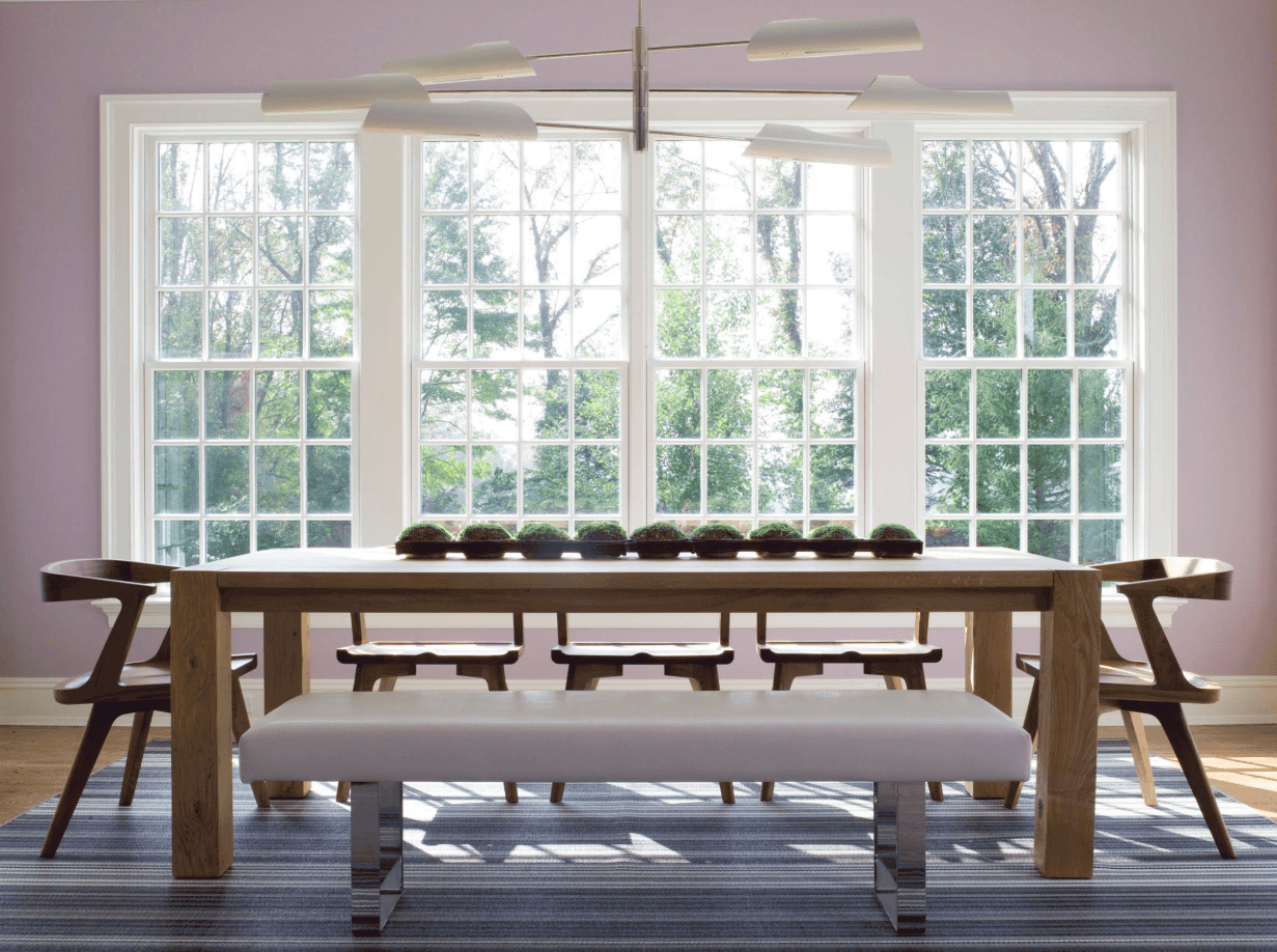 这个餐厅的木桌放在一个大地毯上。宽大的落地窗让阳光照进来，给房间带来温暖明亮的氛围。