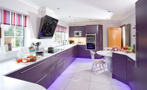 这间厨房以光滑的白色台面和白色瓷砖地板为特色。厨房的柜台和橱柜都是紫色的。