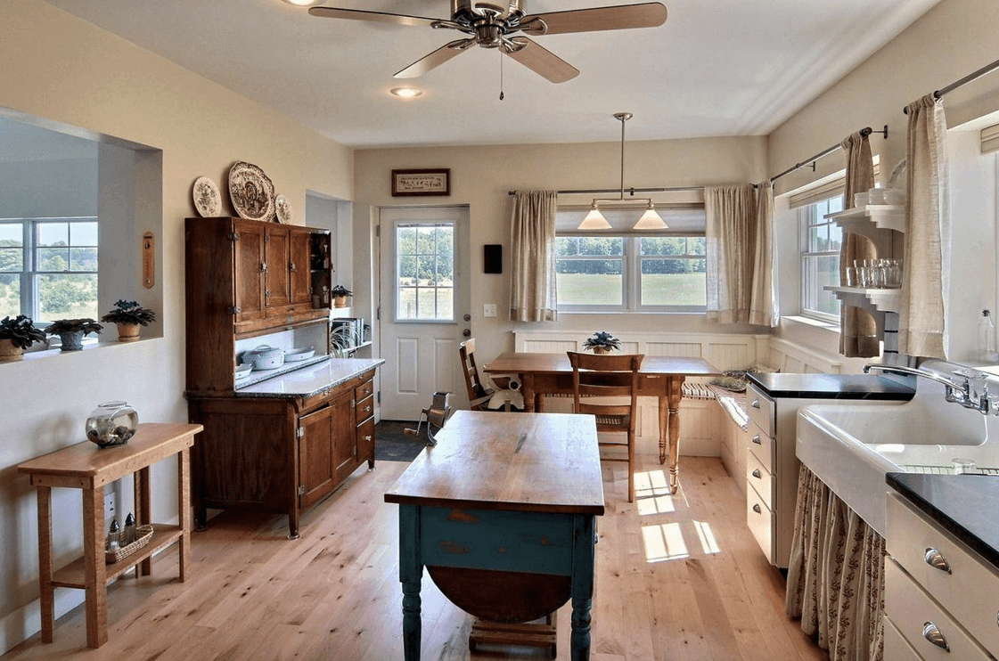 一间可用餐的厨房，有一个靠玻璃窗的用餐角落，设有白色珠板座椅和一张配有配套椅子的木制餐桌。