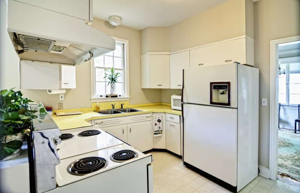 u形厨房，白色橱柜和电器，黄色台面配有不锈钢双水槽。