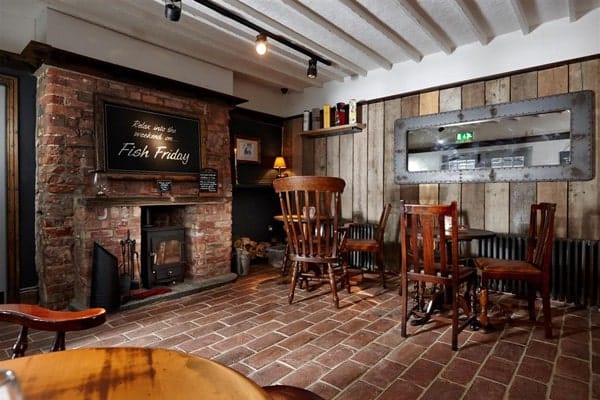 一个质朴的用餐区，有一座砖砌壁炉、质朴的餐桌和再生砖陶土瓷砖地板。