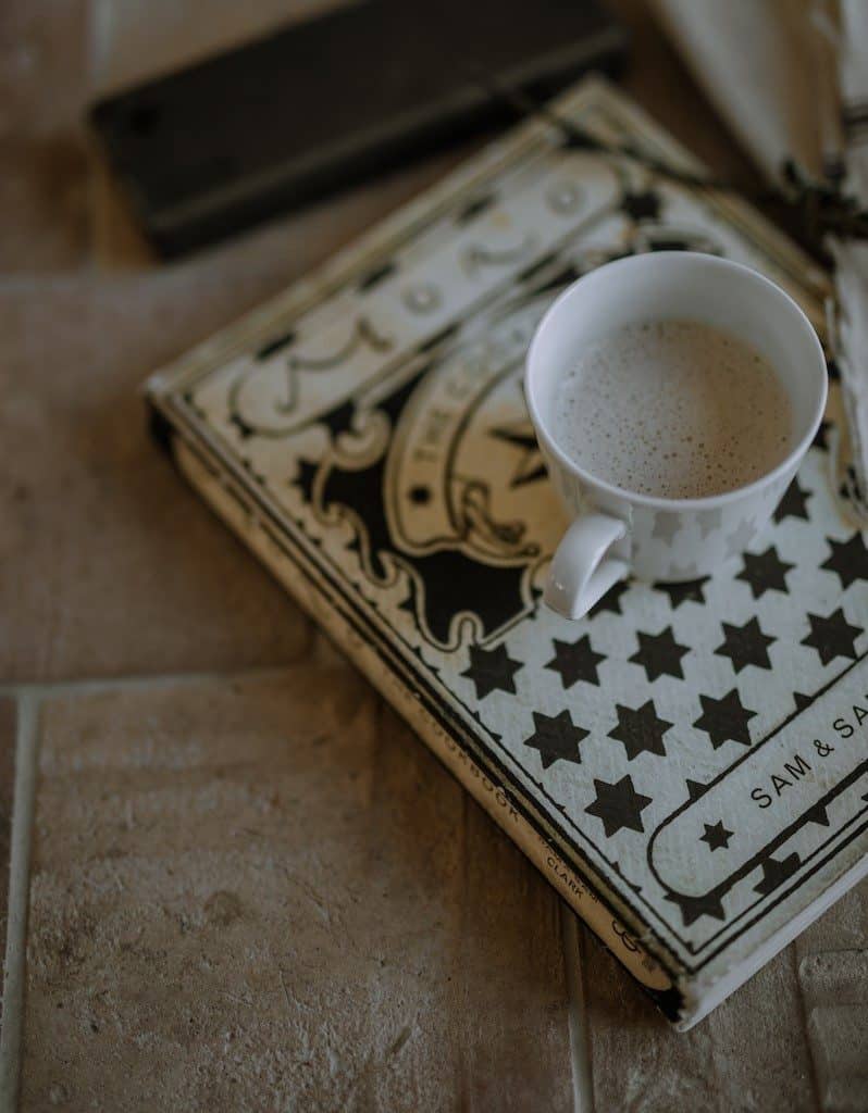 方形的赤陶瓷砖地板，上面放着一本书，书上面放着一杯咖啡。