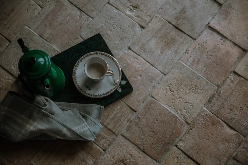 方形的浅色陶土瓷砖地板，上面放着一个茶杯和一个水壶。