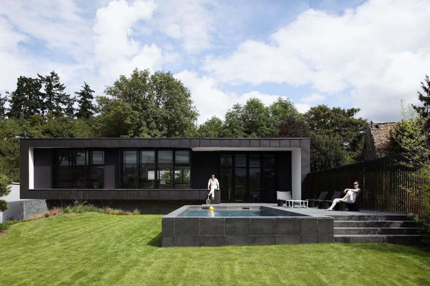 一个黑色的现代住宅，设有游泳池，休息区和维护良好的草坪区。