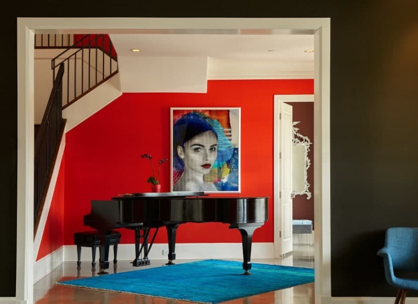 一个优雅的红色门厅与白色口音，设有大型艺术肖像墙装饰和一架黑色钢琴。