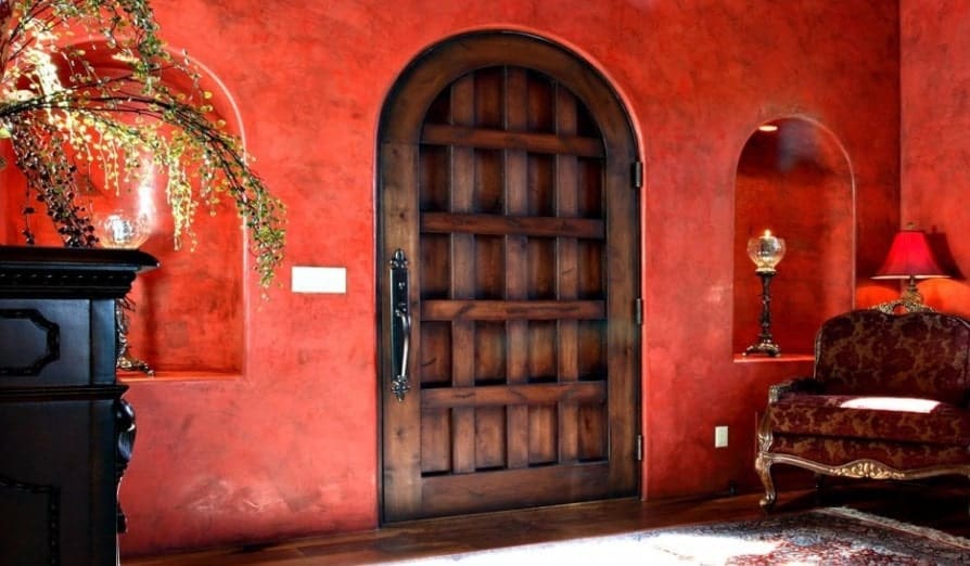 门厅里有红墙和一扇与硬木地板相匹配的乡村门。角落里有一把红椅子，亮着一盏红色的灯。