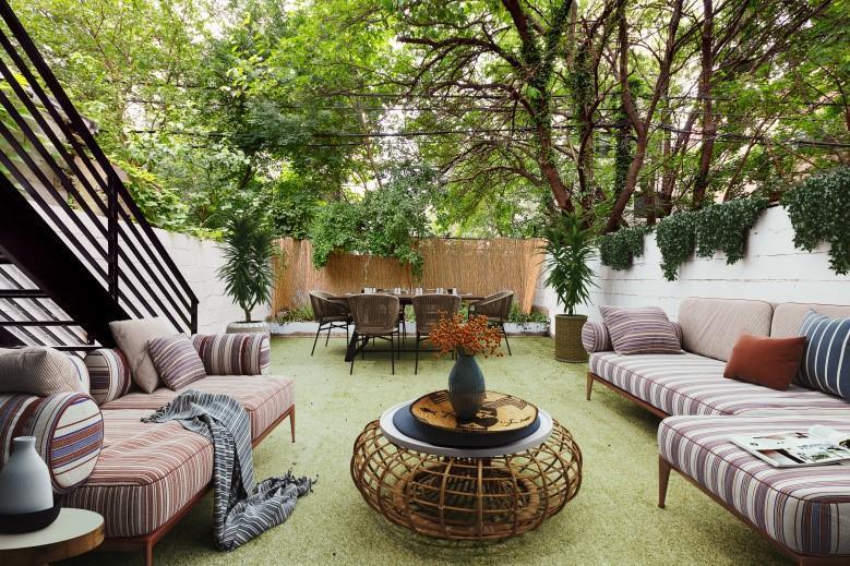 这个令人放松的斯堪的纳维亚风格景观，在乡村木茶几的两侧有一对大软垫沙发。在修剪整齐的草坪的另一端，是一个户外用餐区，配有质朴的椅子，两侧种植着盆栽。