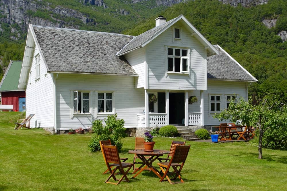 房子的白色外墙是斯堪的纳维亚风格景观的迷人背景，前院的草坪维护得很好。除了一棵中等大小的树外，还有一个户外用餐区，周围有木制折叠椅，围绕着一张同样制作的圆形桌子。