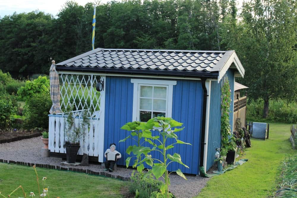 这座小而简单的蓝色房子与周围的斯堪的纳维亚风格景观融为一体，在砾石小径旁边铺着精心修剪的草坪。还有一株蔓生植物爬上了房子蓝色墙壁的一侧。