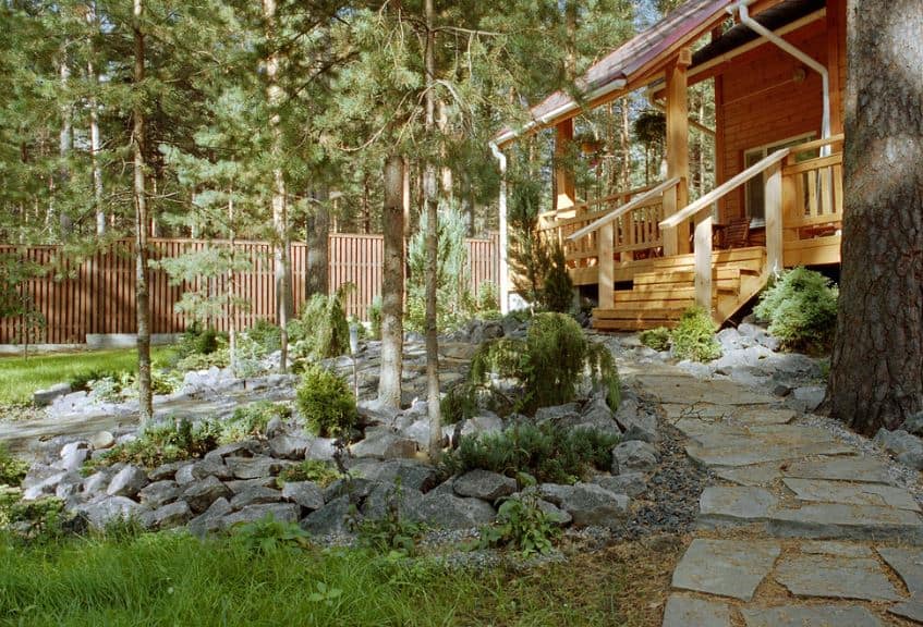 这座迷人的木制小屋周围环绕着斯堪的纳维亚风格的景观，与周围高大的松树和灌木丛相辅相成。有一条嵌入土壤的石头走道通向房子的木制楼梯。