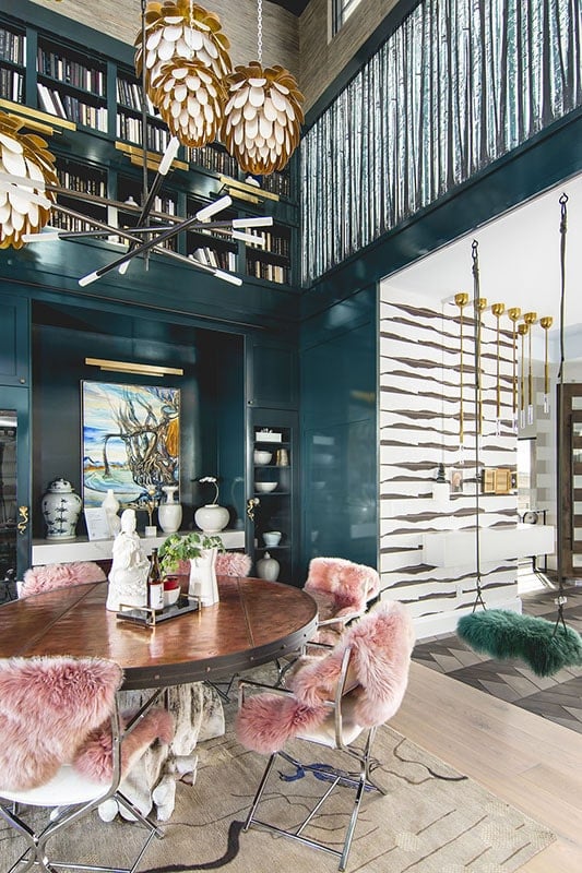 豪华的餐厅，大胆的蓝绿色墙壁与黄铜吊坠和粉红色的人造皮毛覆盖装饰金属扶手椅完美搭配。