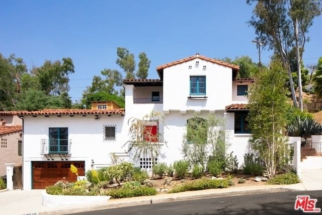 这座西班牙风格住宅的简单白色墙壁与蓝色的法式门窗形成了鲜明的对比。粘土瓦屋顶与木制车库门和景观景观相匹配，呈现出浪漫的西班牙风景。
