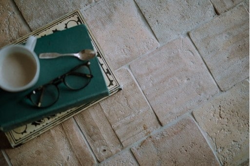 一杯咖啡旁边一茶匙和老花镜一堆书躺在再生砖瓷砖地板。