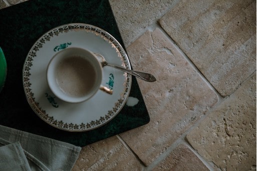 一杯茶和茶匙放在一个碟子上，放在再生瓷砖地板上。