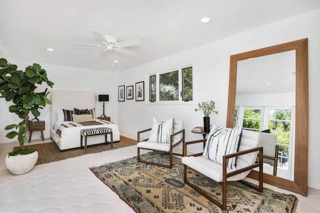 这个西班牙风格的卧室有丰富的图案，从它的区域地毯，枕头和床脚的长凳。室内的植物和巨大的镜子为白色的墙壁和白色的天花板增添了一定的活力，角落里的灯和白色的吊扇。
