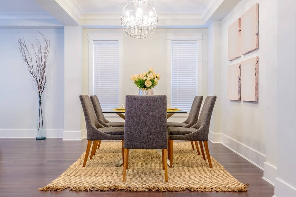 白色的用餐空间以玻璃餐桌为特色，搭配灰色的现代椅子，棕色的地毯覆盖着硬木地板。