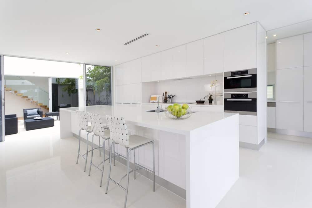 这个厨房的一致性和简单的白色亮度在白色的单调中几乎是临床的。白色厨房岛台的现代烤箱和现代钢凳稍微缓和了这种感觉。巨大的玻璃门的外部景观也平衡了这一点。