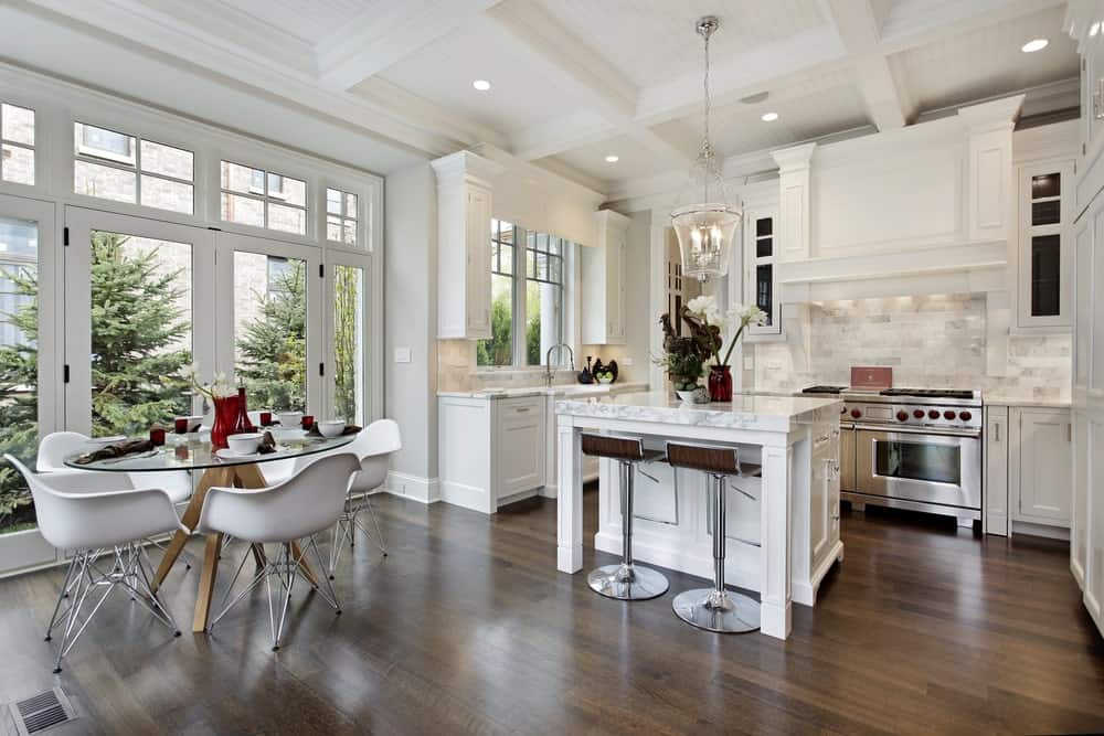 厨房的白色格子天花板与小而私密的用餐区共享。另一方面，玻璃门和窗户让自然光照射在硬木地板上，让白色的厨房岛式和半岛式显得格外突出。