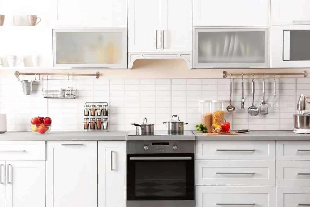 这是白色烹饪区域的特写，后挡板的白色瓷砖上方有一丝粉米色。这个厨房半岛的台面是浅灰色的，与烤箱、抽屉和橱柜的固定装置相匹配。
