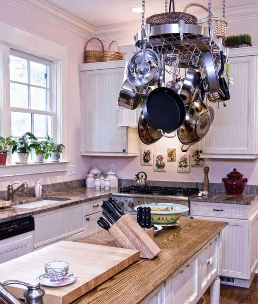 白色的厨房里有珠板橱柜和一个椭圆形的锅架，它兼作架子，悬挂在木制厨房岛台上。