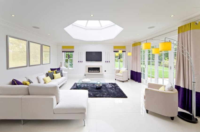 白色的客厅以黄色和紫色为主调。它有一个带天窗的天花板，还有一个壁炉，上面有一台电视。