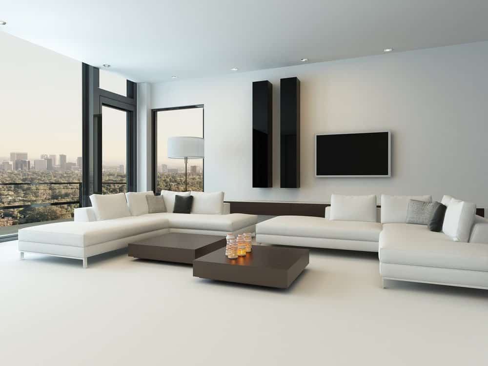 大型现代客厅，白色地板上有白色l形沙发。中间的桌子看起来绝对时髦。墙上还有一台电视。