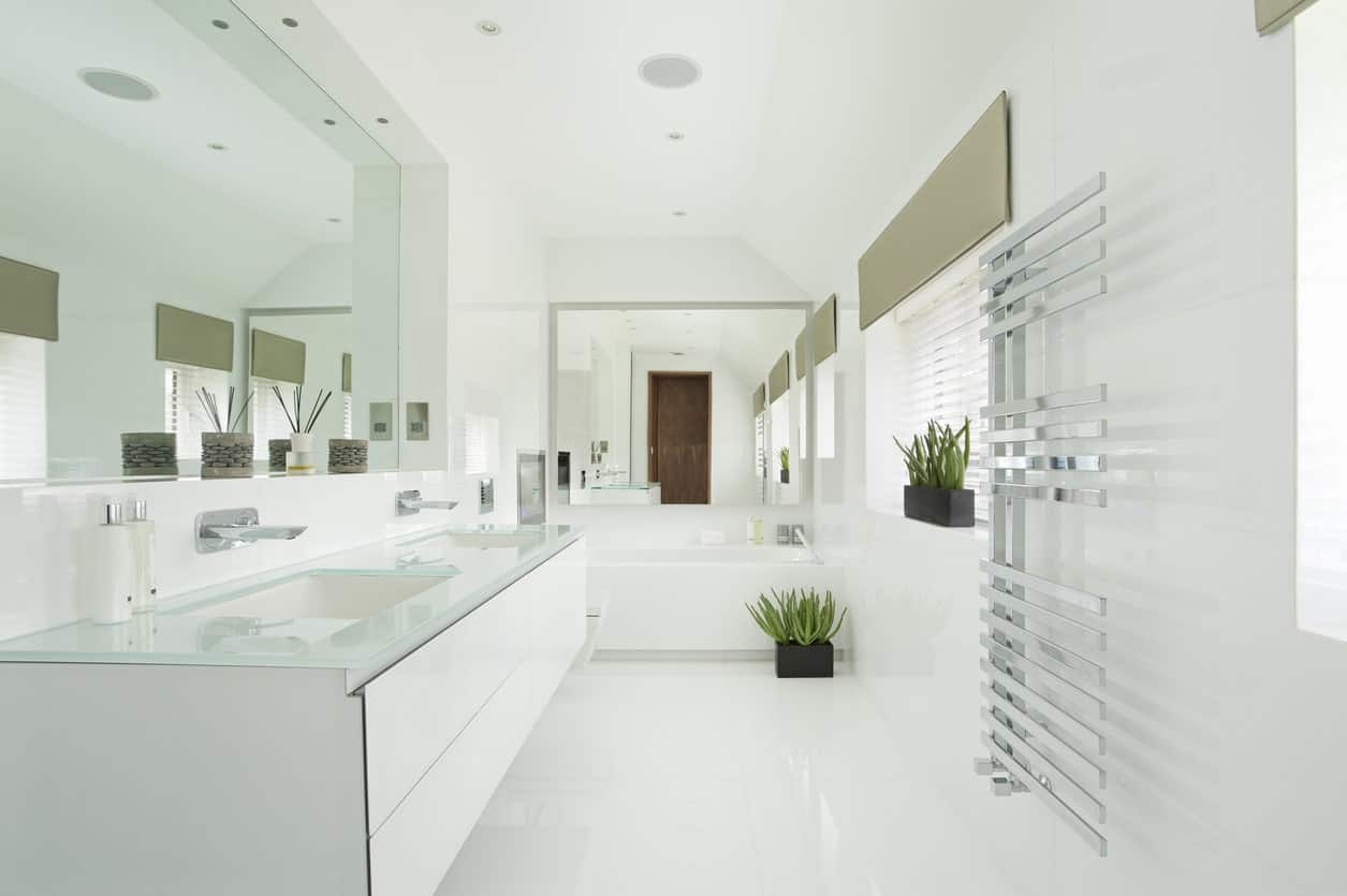 时尚的主浴室设有带两个水槽的玻璃水槽台面。角落里有个临时浴缸。这里还有一对盆栽植物，为这个白色主题的浴室增添了色彩。