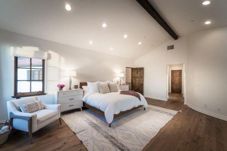 极简主义的主卧室以白色墙壁和质朴的硬木地板为特色。房间里有嵌入式灯和台灯照明。