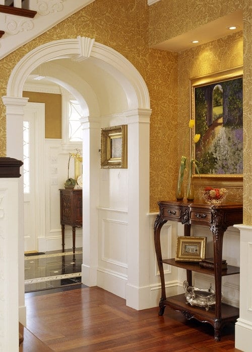 维多利亚式的门厅覆盖着黄色的碎花壁纸，强调了一个可爱的墙壁艺术安装在木制控制台桌上。