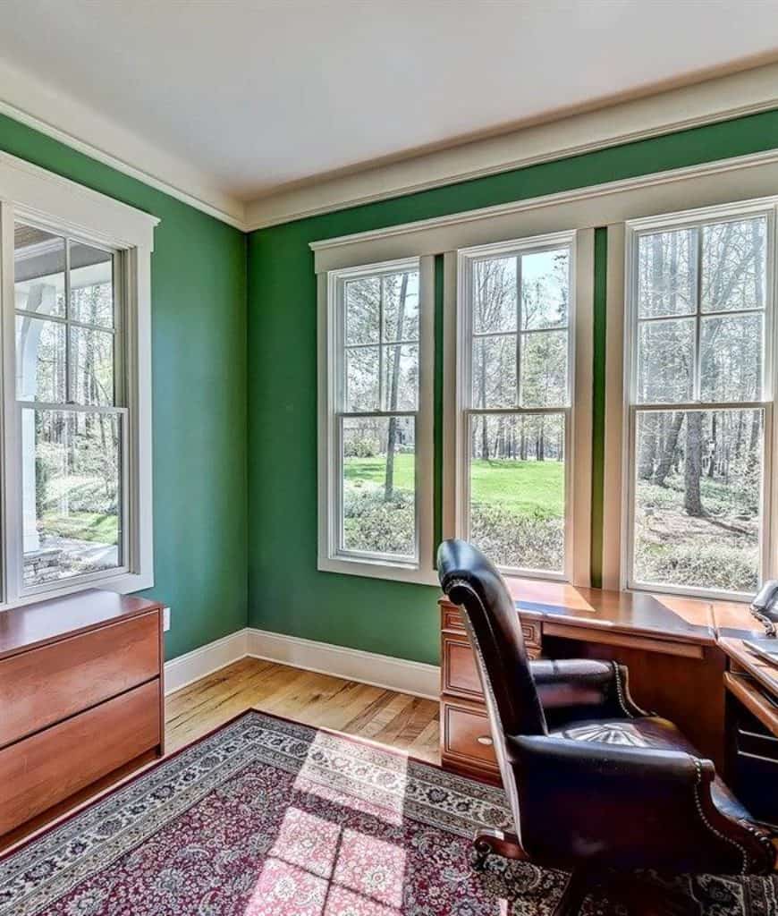 传统的家庭办公室，经典的区域地毯和木制办公桌搭配皮革办公椅。它有观景窗，可以俯瞰长满参天大树的迷人庭院。
