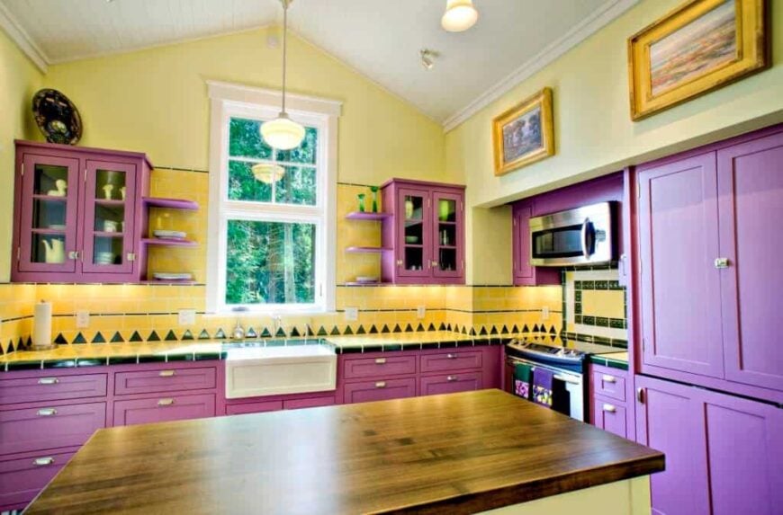 黄色的厨房中夹杂着紫色的色调。橱柜、置物架和厨房柜台搭配在一起。中心岛有一个厚木板顶部。