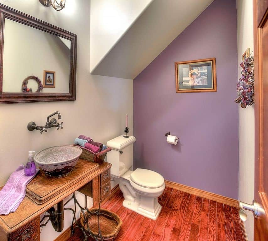 小主浴室有一个经典的复古水槽，以及丰富的硬木地板和一面紫色的墙。