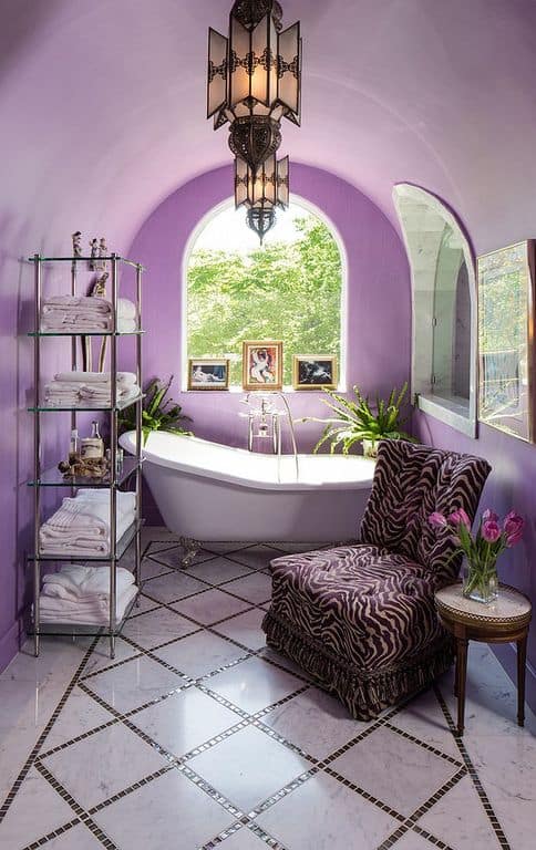 优雅的主浴室环绕着紫色的墙壁和天花板。它有漂亮的瓷砖地板，一个独立的浴缸和一把漂亮的椅子。