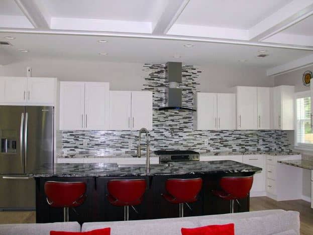 红色的翼背凳子和黑色的厨房岛是这个白色厨房的中心，有白色的摇床柜和抽屉。
