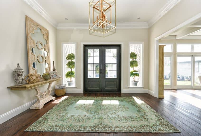 这个门厅的亮点是明亮而欢快的浅绿色图案地毯覆盖着硬木地板。这与一个弯曲的米黄色控制台桌子搭配，上面有各种装饰品，还有一个与灯笼吊灯相匹配的大镜子。